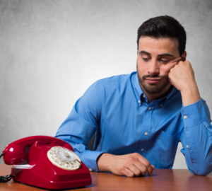 Man wearing bright blue shirt, looking puzzled at red telephone waiting for it to ring.